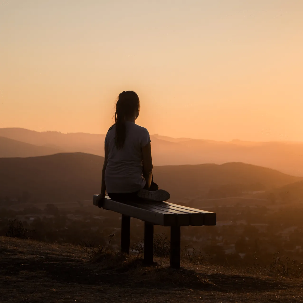 A person sitting outdoors at sunset, reflecting